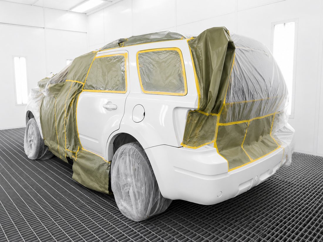 La misma camioneta en la cabina de pintura, con el costado recién pintado y el resto protegido